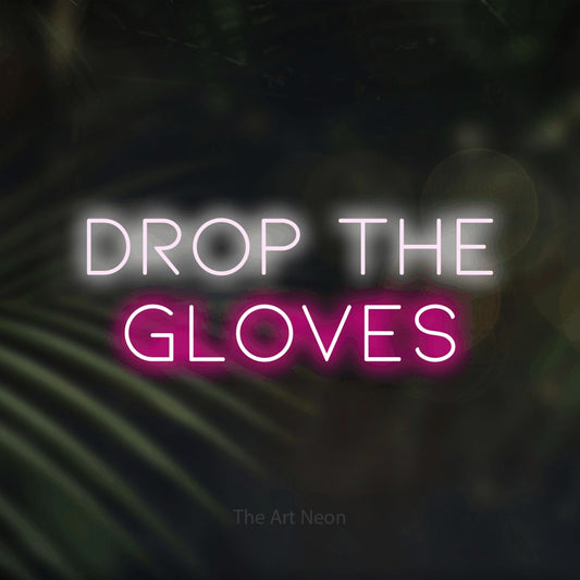 Hot pink and cool white LED neon sign reading "Drop the Gloves" against dark blurred palm leaves