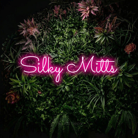 Hot pink LED neon sign reading "Silky Mitts" against a flowering garden wall