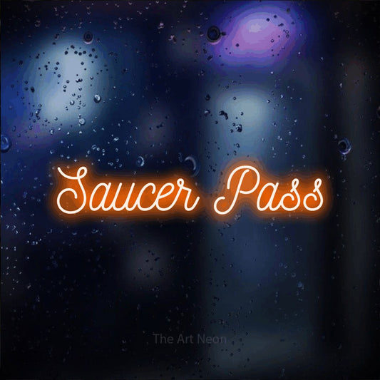 Orange script-style LED neon sign reading "Saucer Pass" against a dark blue bokeh background