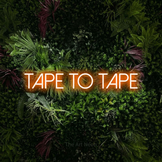 Orange LED neon sign reading "Tape to Tape" against a lush garden wall with pink flowers