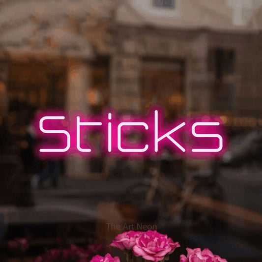 Hot pink LED neon sign reading "Sticks" in a softly blurred café interior