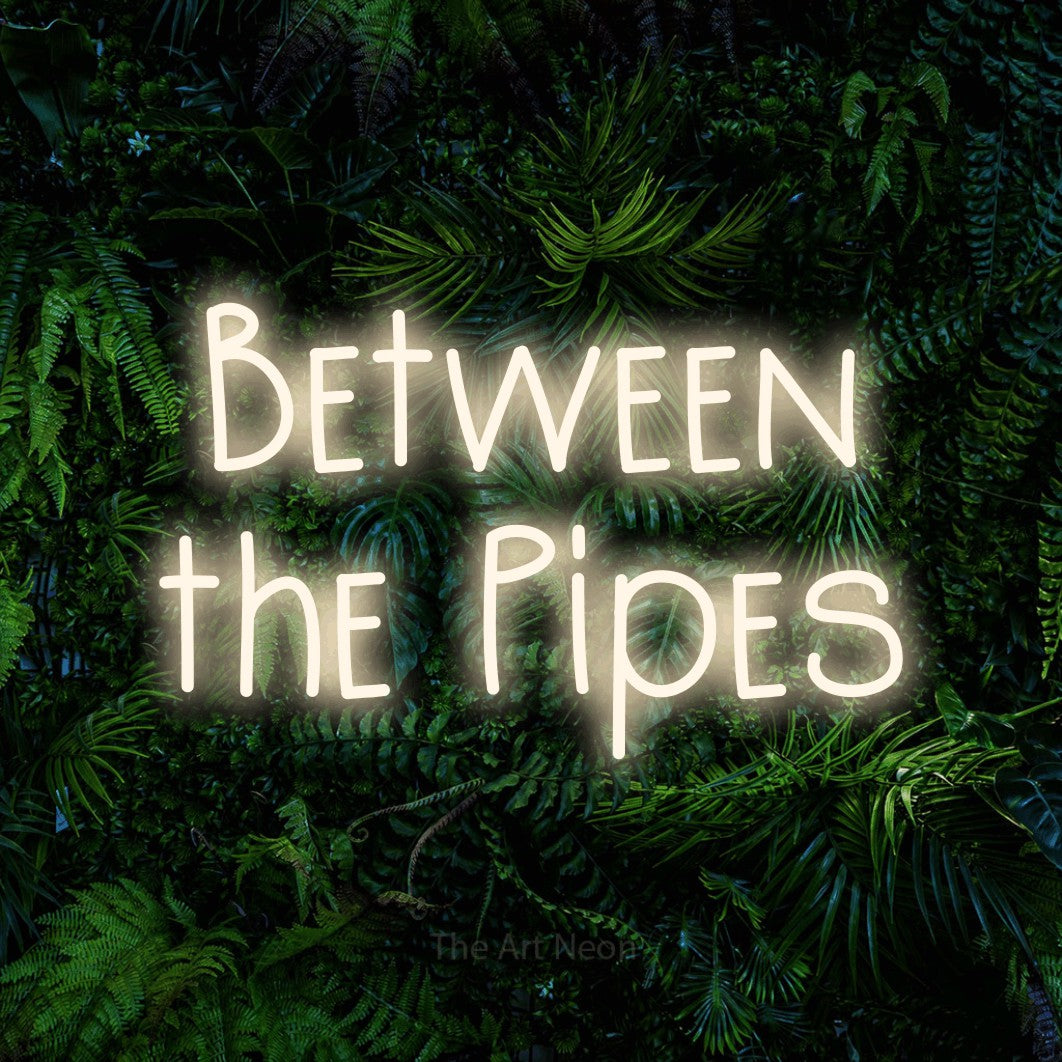 Warm white LED neon sign reading "Between the Pipes" against a dense tropical foliage wall