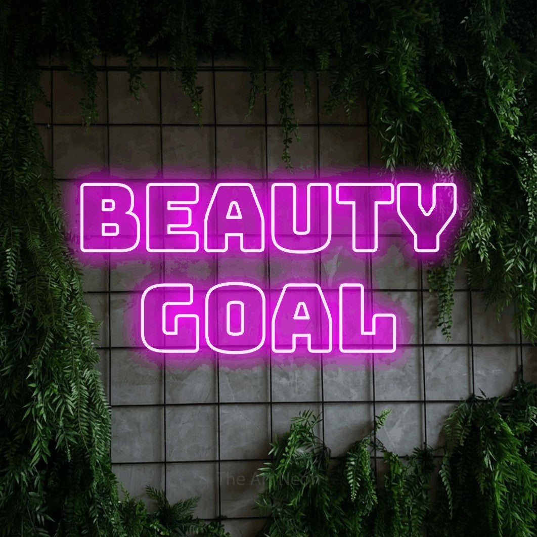 Pink outline-style LED neon sign reading "Beauty Goal" against a green grid wall with foliage