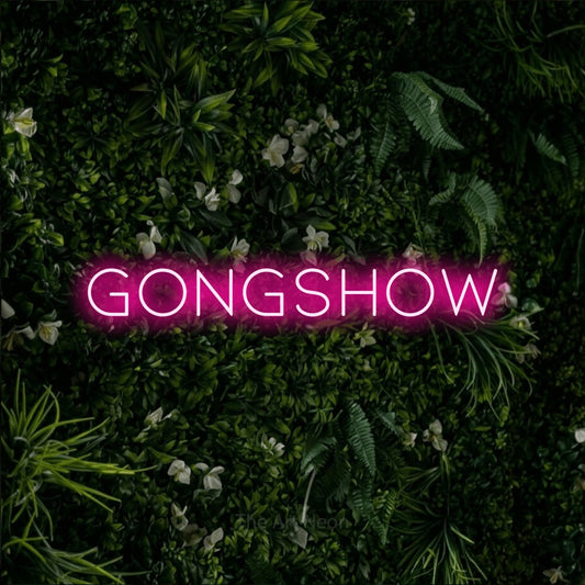 Enseigne néon à DEL à lumière rose vif, affichant « Gongshow » sur un mur de feuillage vert