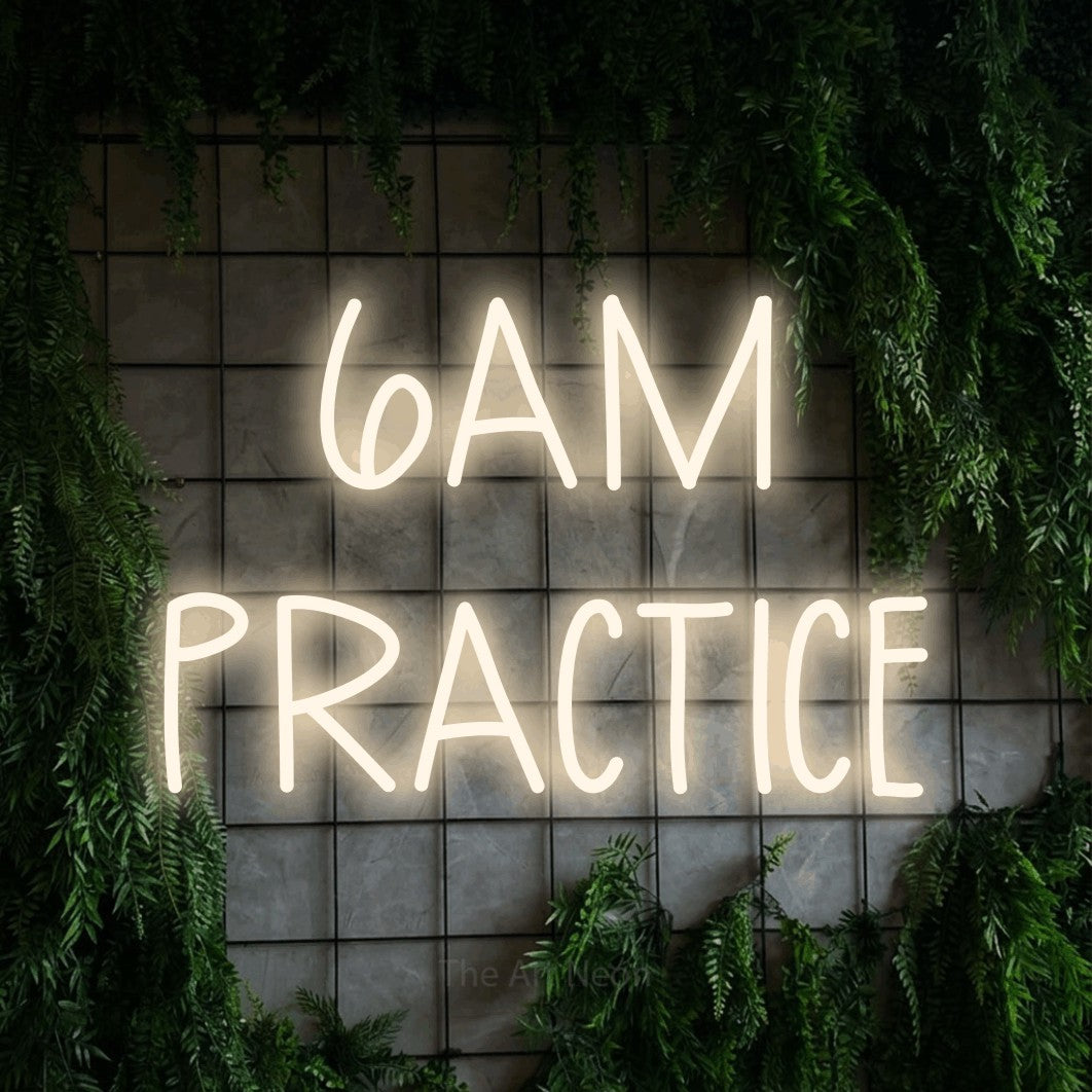 Enseigne néon à DEL à lumière blanche chaude, affichant « 6AM Practice » sur un mur quadrillé vert avec du feuillage