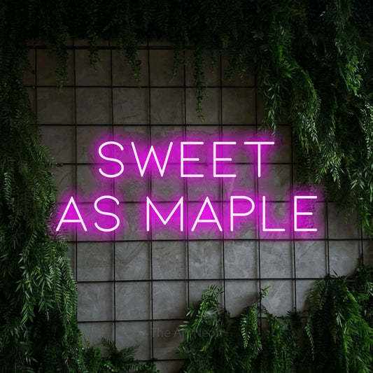 Enseigne néon à DEL à lumière rose, affichant « Sweet as Maple » sur un mur quadrillé vert avec du feuillage