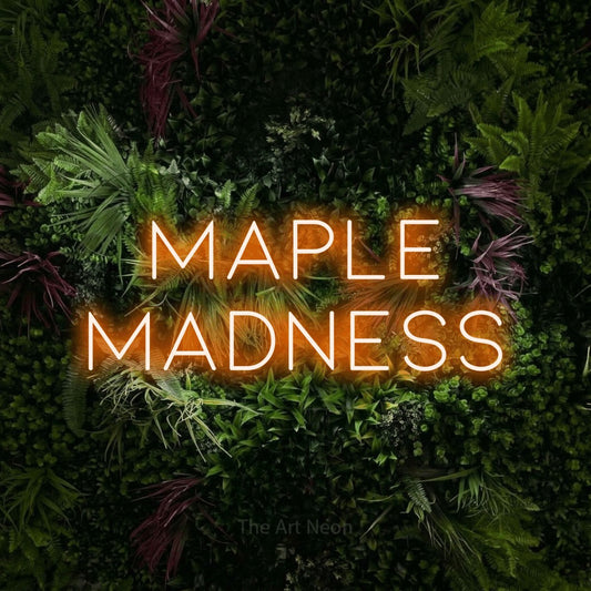 Enseigne néon à DEL à lumière orange, affichant « Maple Madness » sur un mur de jardin luxuriant aux fleurs roses