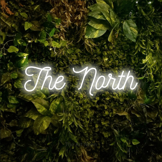 Enseigne néon à DEL à lumière blanche froide, de style manuscrit, affichant « The North » sur un mur texturé de mousse et de feuillage