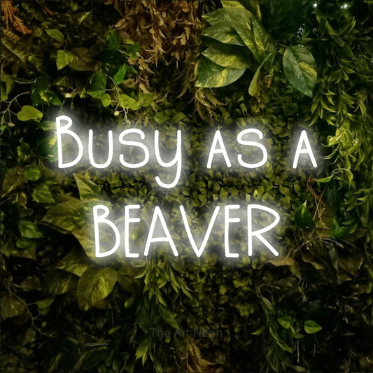 Enseigne néon à DEL à lumière blanche froide, affichant « Busy as a Beaver » sur un mur texturé de mousse et de feuillage