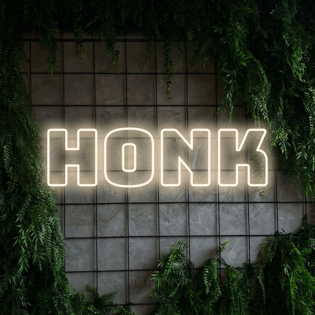 Enseigne néon à DEL à lumière blanche chaude, de style contour, affichant « Honk » sur un mur quadrillé vert avec du feuillage