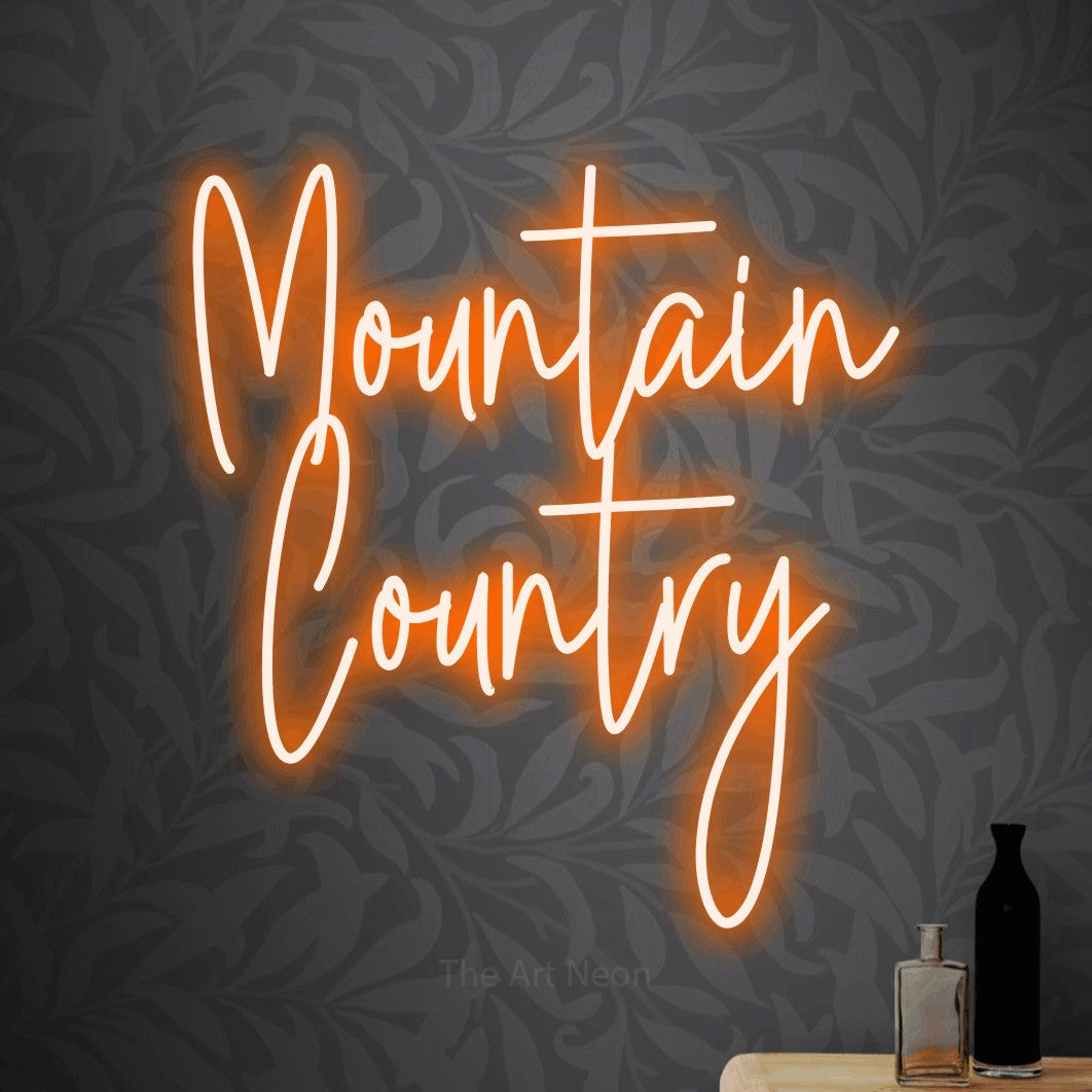Orange script-style LED neon sign reading "Mountain Country" against light grey floral wallpaper