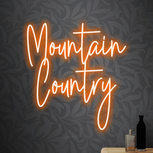 Orange script-style LED neon sign reading "Mountain Country" against light grey floral wallpaper