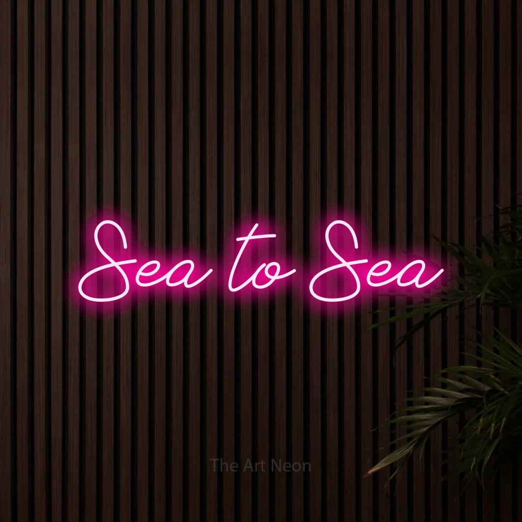 Hot pink script-style LED neon sign reading "Sea to Sea" against dark wooden slats