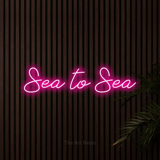 Hot pink script-style LED neon sign reading "Sea to Sea" against dark wooden slats