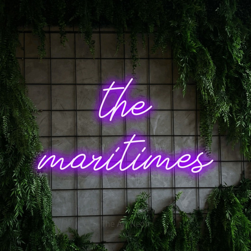 Purple script-style LED neon sign reading "The Maritimes" against a green grid wall with foliage