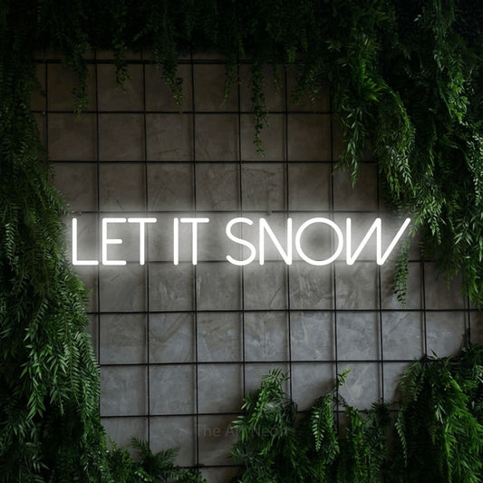Cool white LED neon sign reading "Let It Snow" against a green grid wall with foliage