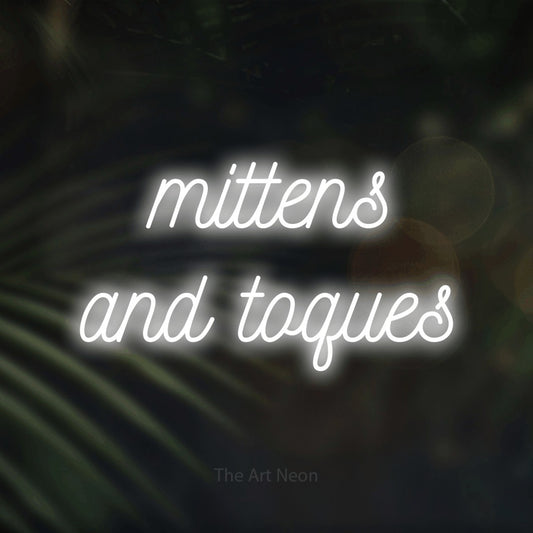 Enseigne néon à DEL à lumière blanche froide, de style manuscrit, affichant « Mittens and Toques » sur des feuilles de palmier foncées et floues