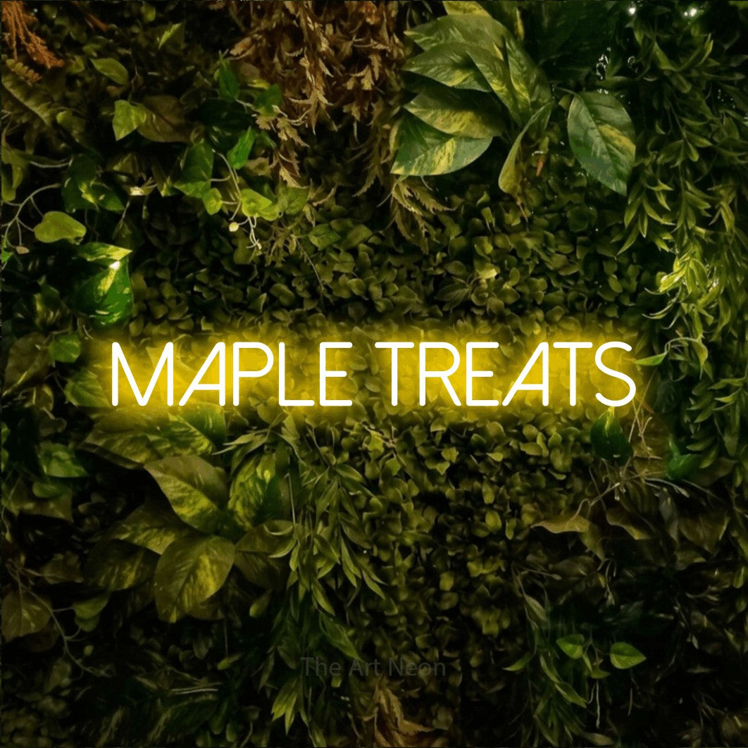 Yellow LED neon sign reading "Maple Treats" against a textured moss and foliage wall