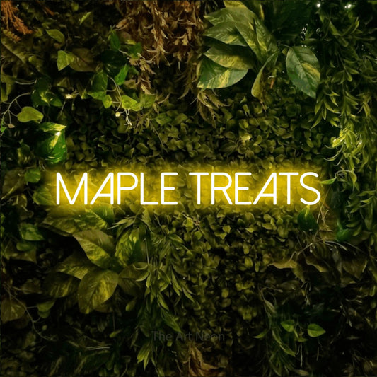 Enseigne néon à DEL à lumière jaune, affichant « Maple Treats » sur un mur texturé de mousse et de feuillage