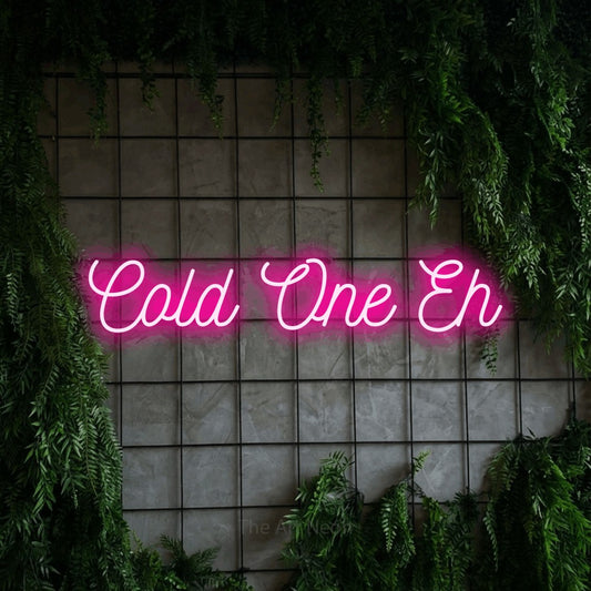 Hot pink script-style LED neon sign reading "Cold One Eh" against a green grid wall with foliage