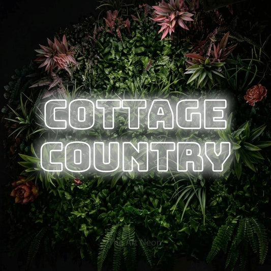 Cool white outline-style LED neon sign reading "Cottage Country" against a flowering garden wall