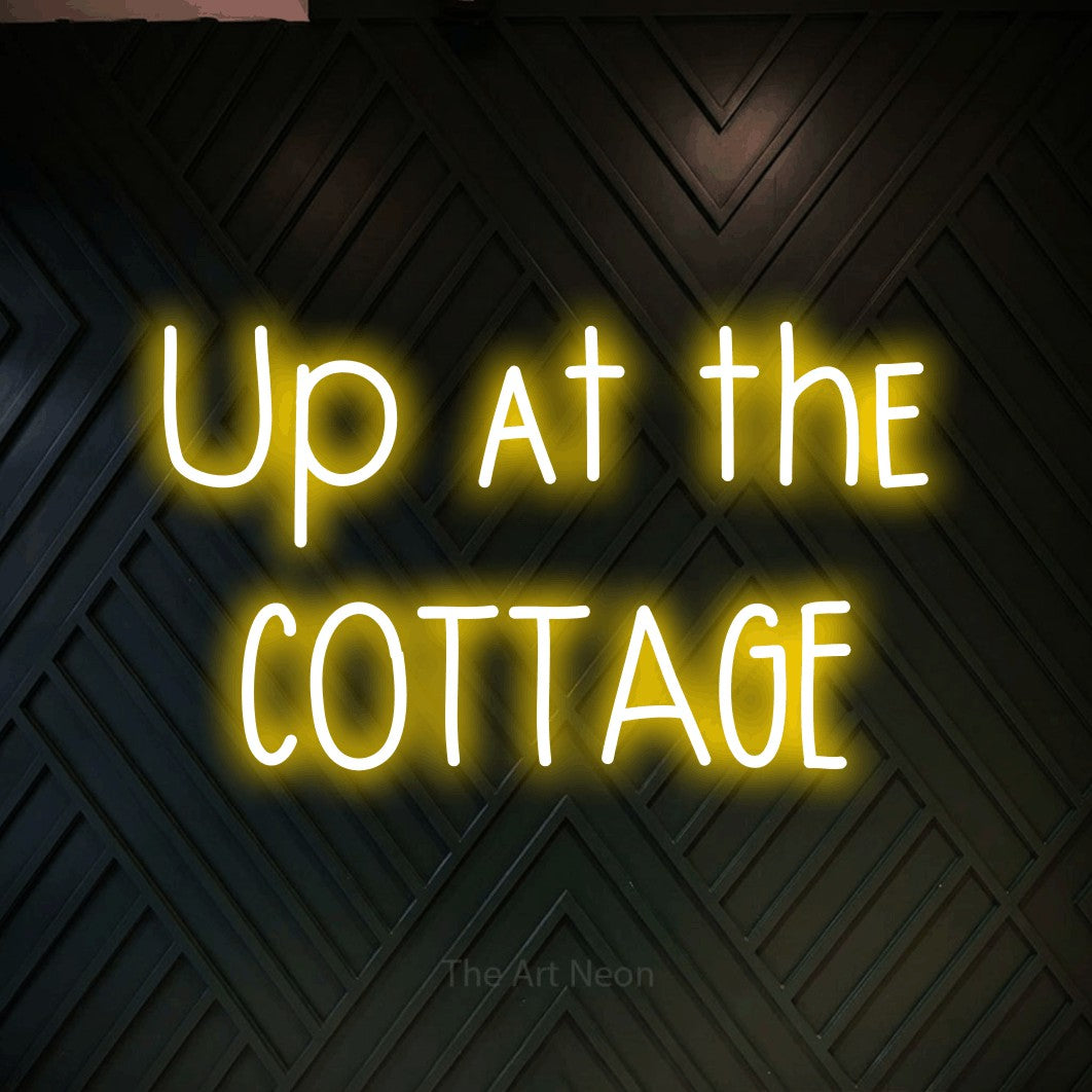 Yellow LED neon sign reading "Up at the Cottage" against a dark geometric wood wall