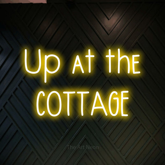 Yellow LED neon sign reading "Up at the Cottage" against a dark geometric wood wall