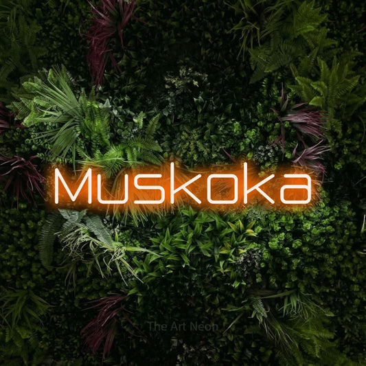 Orange LED neon sign reading "Muskoka" against a lush garden wall with pink flowers