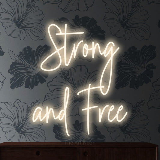 Warm white script-style LED neon sign reading "Strong and Free" against grey floral wallpaper