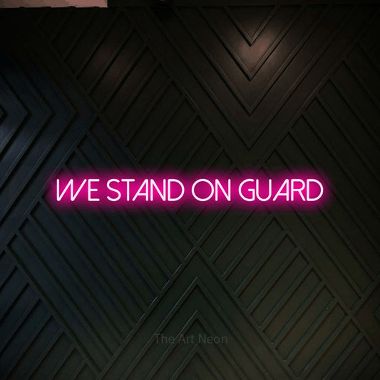 Hot pink LED neon sign reading "We Stand on Guard" against a dark geometric wood wall