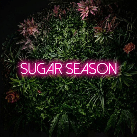 Hot pink LED neon sign reading "Sugar Season" against a flowering garden wall
