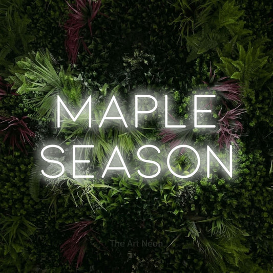 Cool white LED neon sign reading "Maple Season" against a lush garden wall with pink flowers