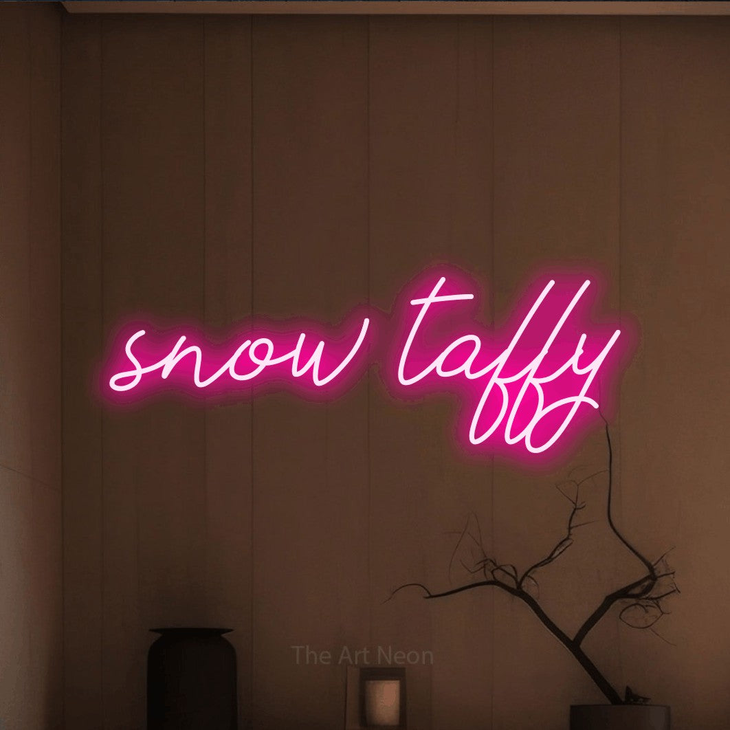 Hot pink script-style LED neon sign reading "Snow Taffy" against a warm brown wall