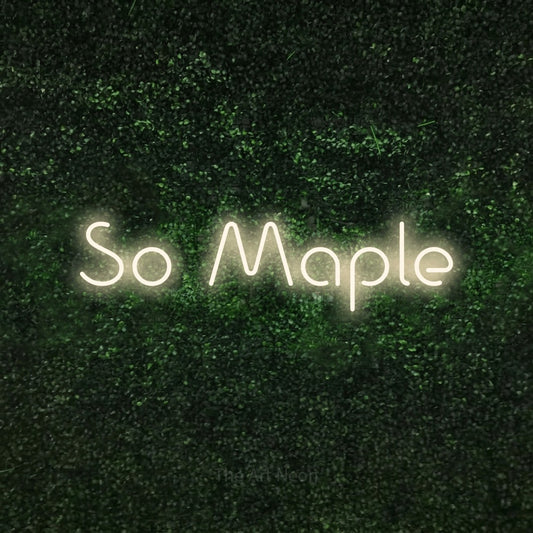 Warm white LED neon sign reading "So Maple" against a textured green moss wall