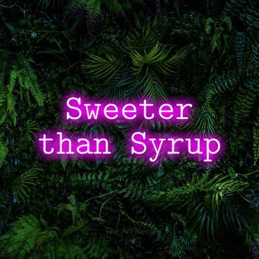 Pink LED neon sign reading "Sweeter than Syrup" against a dense tropical foliage wall