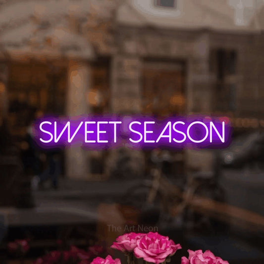 Purple LED neon sign reading "Sweet Season" in a softly blurred café interior