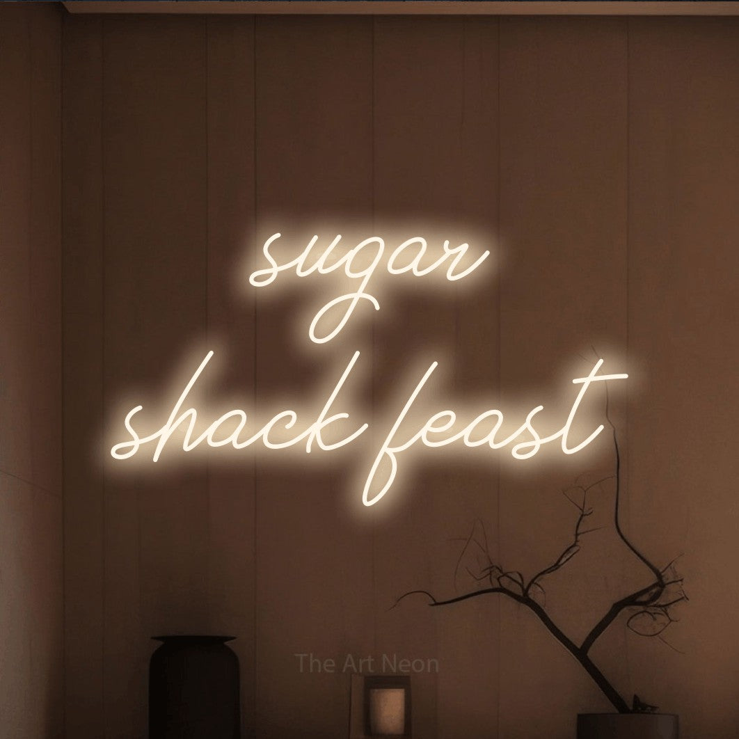 Warm white script-style LED neon sign reading "Sugar Shack Feast" against a warm brown wall