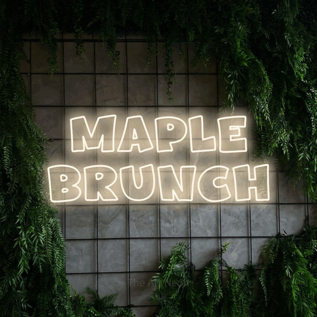 Warm white outline-style LED neon sign reading "Maple Brunch" against a green grid wall with foliage