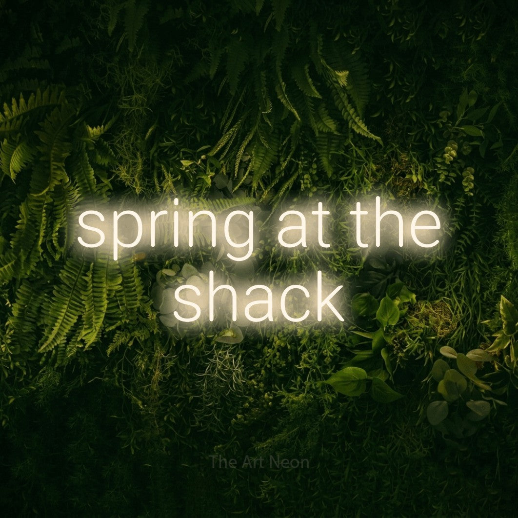 Warm white LED neon sign reading "Spring at the Shack" against a moss-covered green wall