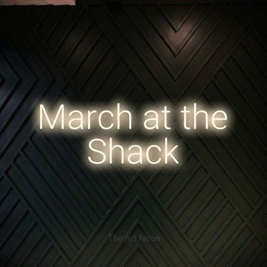 Warm white LED neon sign reading "March at the Shack" against a dark geometric wood wall
