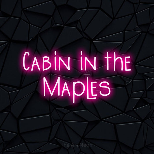Hot pink LED neon sign reading "Cabin in the Maples" against a black faceted wall