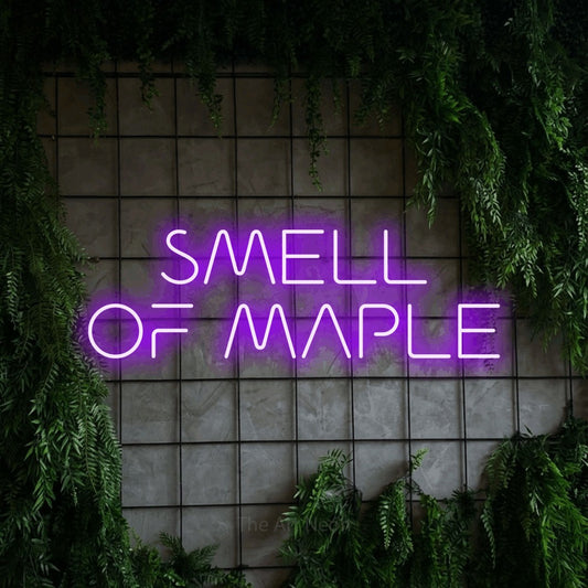 Purple LED neon sign reading "Smell of Maple" against a green grid wall with foliage