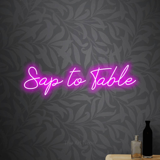 Pink script-style LED neon sign reading "Sap to Table" against light grey floral wallpaper