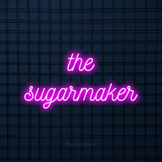 Pink script-style LED neon sign reading "The Sugarmaker" against a dark blue tiled wall