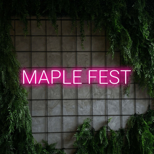 Hot pink LED neon sign reading "Maple Fest" against a green grid wall with foliage