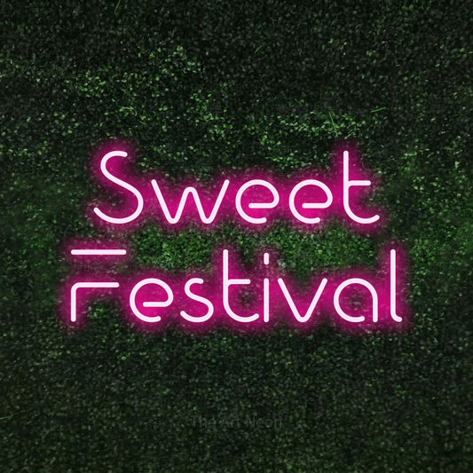 Hot pink LED neon sign reading "Sweet Festival" against a textured green moss wall