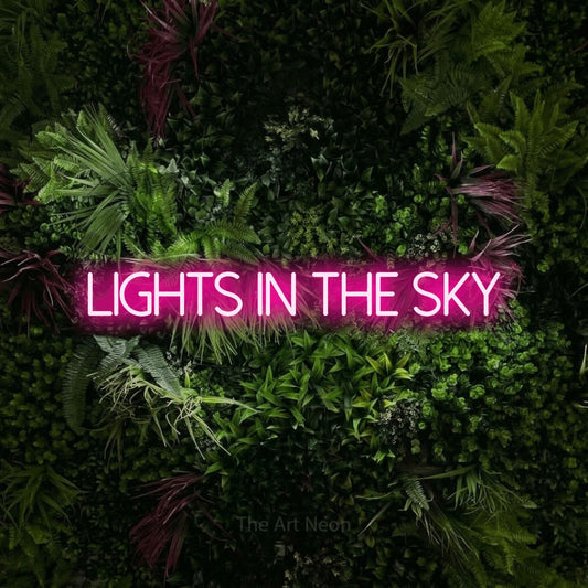 Hot pink LED neon sign reading "Lights in the Sky" against a lush garden wall with pink flowers