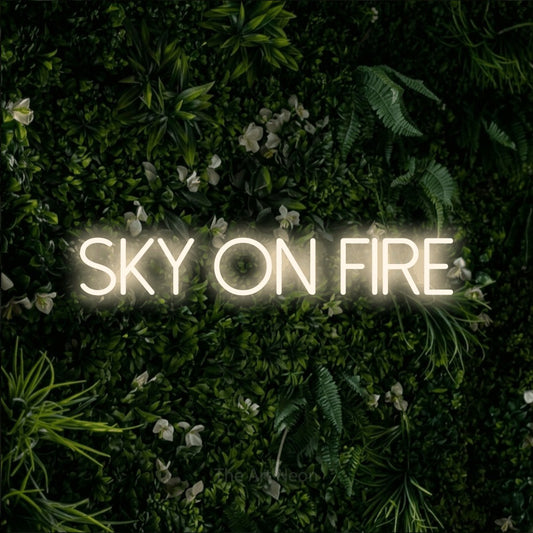 Warm white LED neon sign reading "Sky on Fire" against a leafy green wall