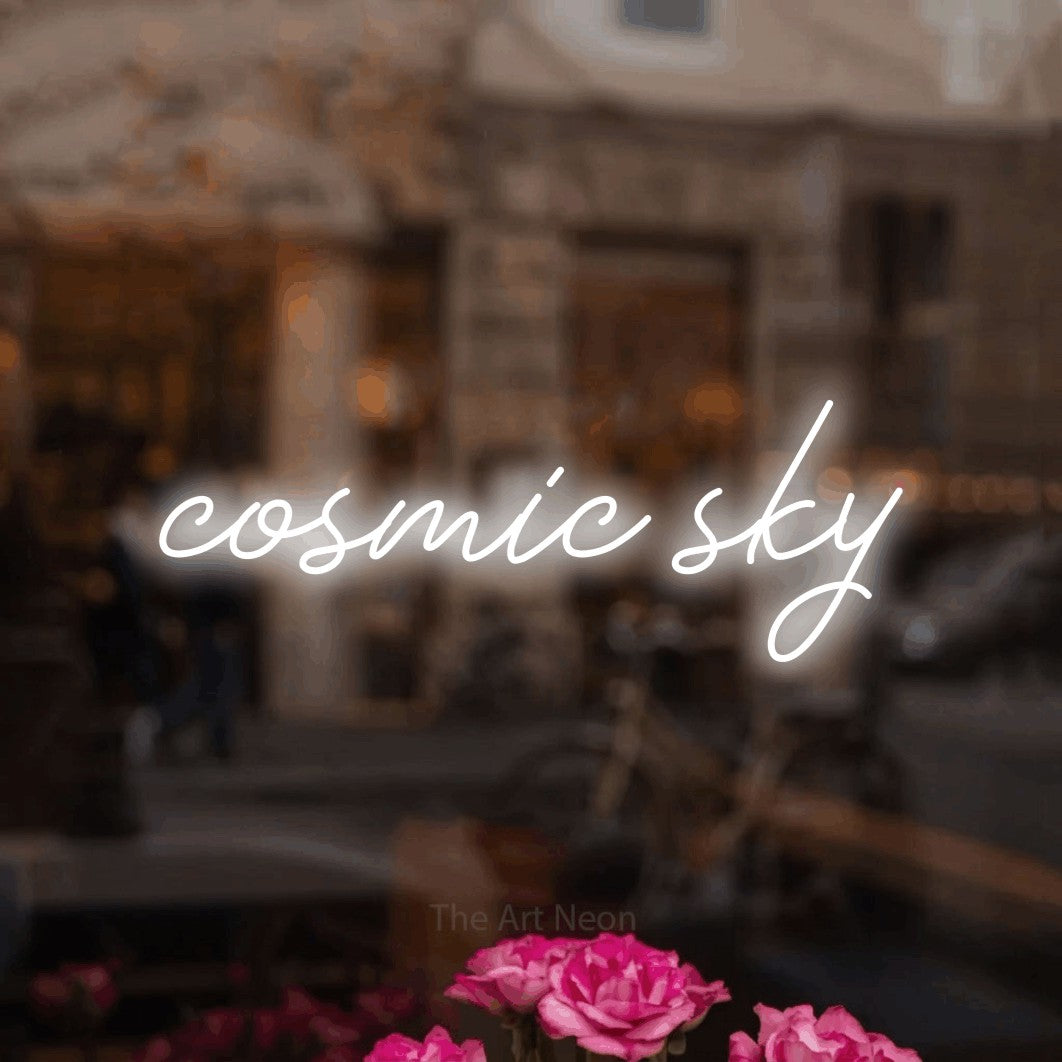 Cool white script-style LED neon sign reading "Cosmic Sky" in a softly blurred café interior