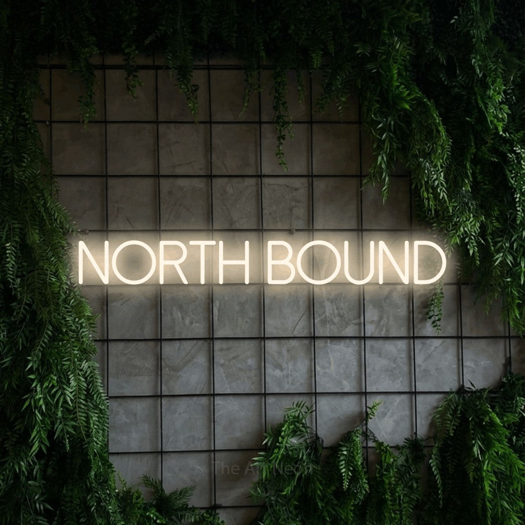 Warm white LED neon sign reading "North Bound" against a green grid wall with foliage